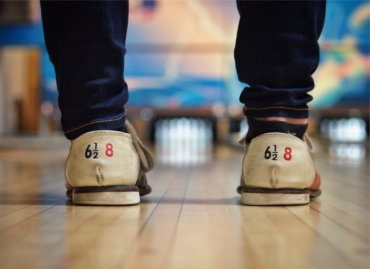 photograph picture of a person wearing bowling shoes standing in front of a bowling lane