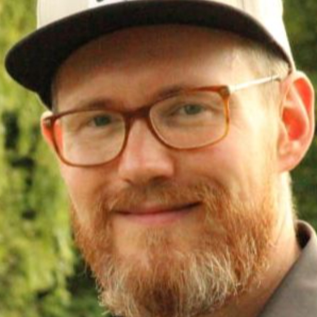 A smiling man with a beard and glasses outdoors