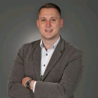 A man in a gray blazer and white shirt with his arms crossed.