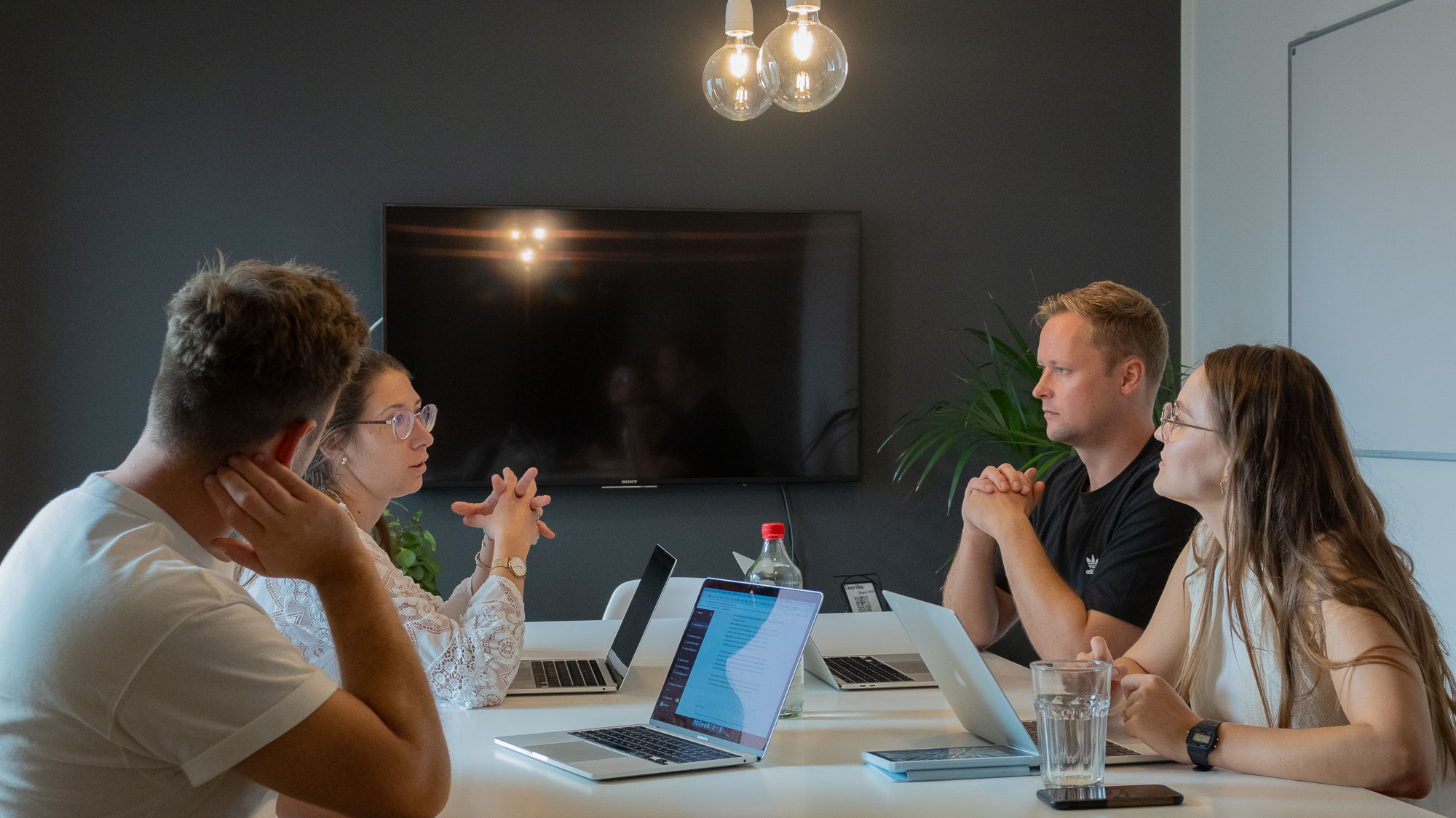 group of people sitting around a table with laptops discussing something, engaged conversation